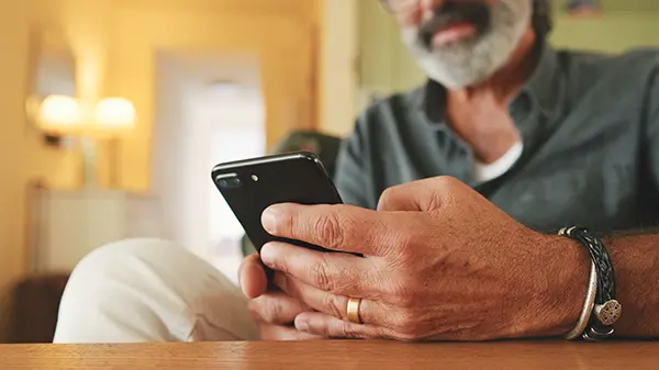 Close-up of an elderly man's hands typing on mobile phone sitting in the kitchen Registering an iCare+ Test Kit