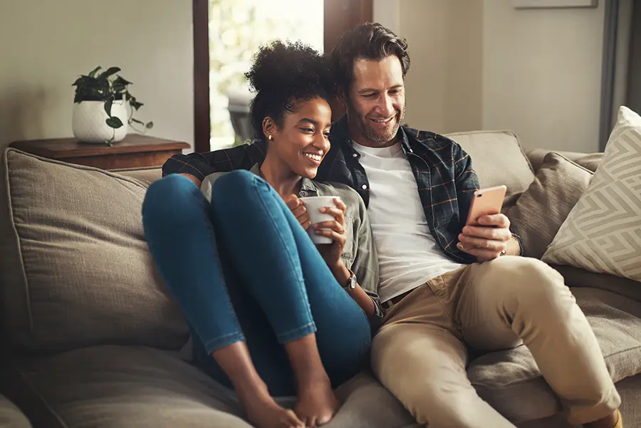 happy young couple using a digital tablet while relaxing on a couch in their living room at home