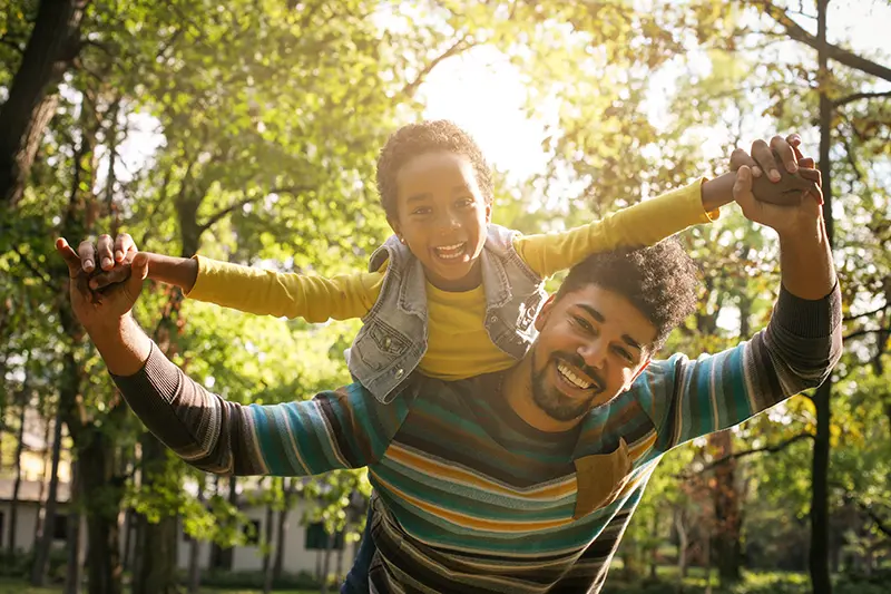 Smiling African American father carrying his daughter on piggyback and holding hands.