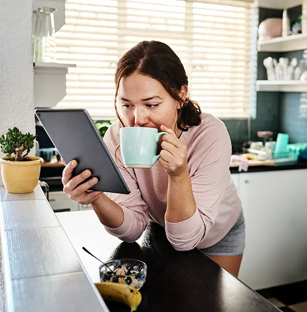 Young woman drinking coffee while using a digital tablet to look at her iCare+ test kit results copy